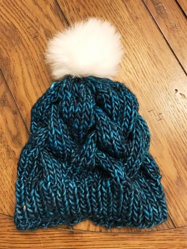 Knitted blue hat with a pompom on the table.
