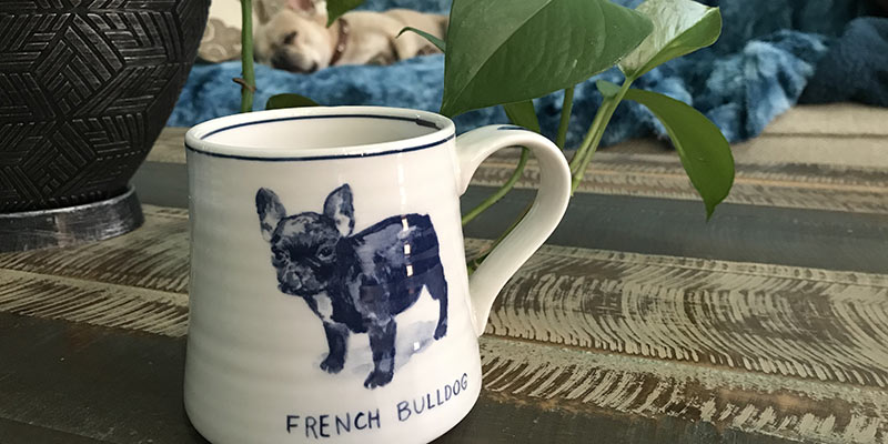 A white ceramic cup with a navy drawing of a dog on it.