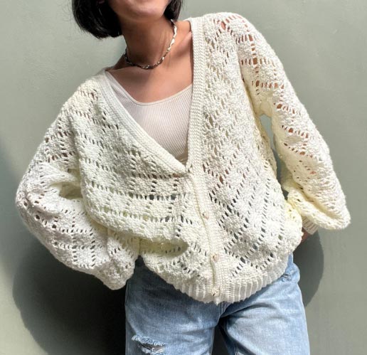 Image of a white cardigan with pattern of medium sized diamonds separated by lace holes.