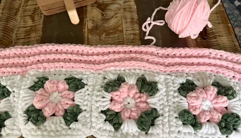 A very plush, crocheted white and pink blanket with pink flowers