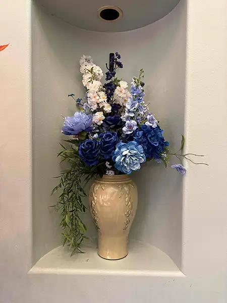 Blue faux flowers in a big vase in a niche in the wall.